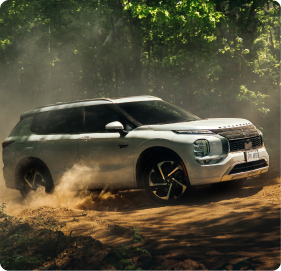 White SUV driving off-road on dusty terrain with green trees in the background.