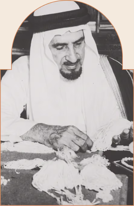 رجل عربي يرتدي الثوب والغترة يعمل على ترتيب خرز أو حبات بيضاء على الطاولة.