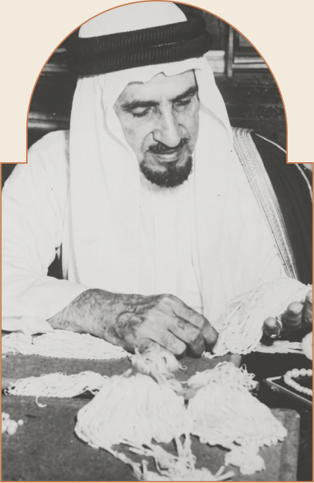 رجل عربي يرتدي الثوب والغترة يعمل على ترتيب خرز أو حبات بيضاء على الطاولة.