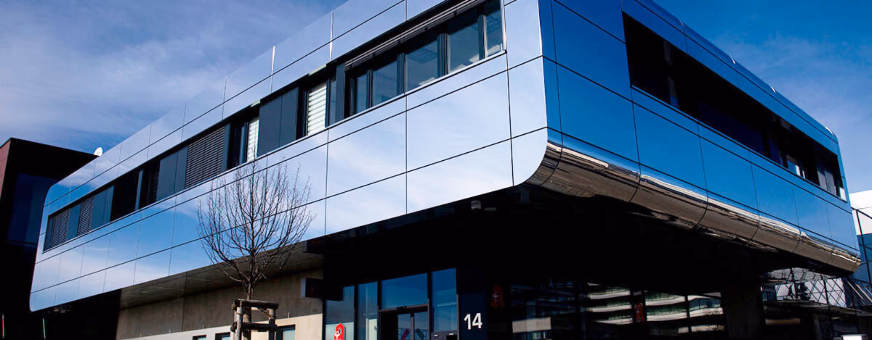 Modernes, kubisches Bürogebäude mit großen Glasfronten und dunklem Unterbau vor blauem Himmel