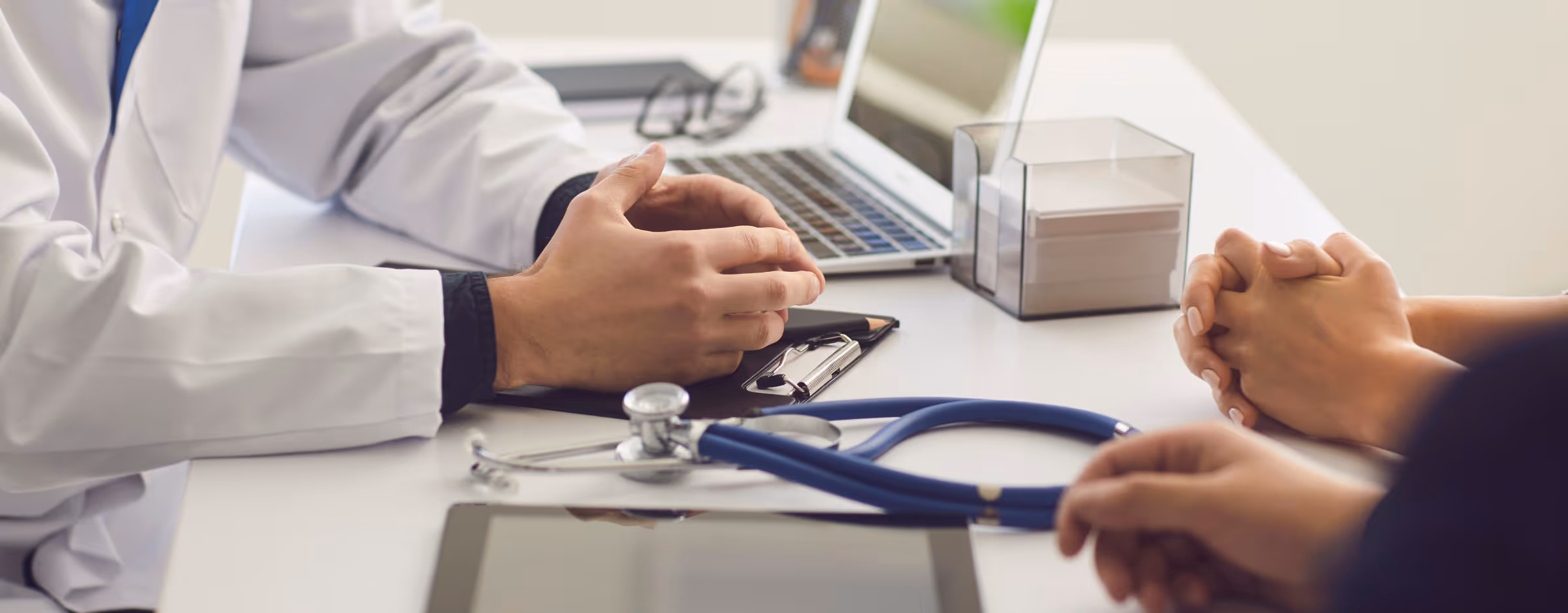 Die Hand eines Arztes und einer Patientin sind zu sehen. Sie sitzen an einem Tisch.