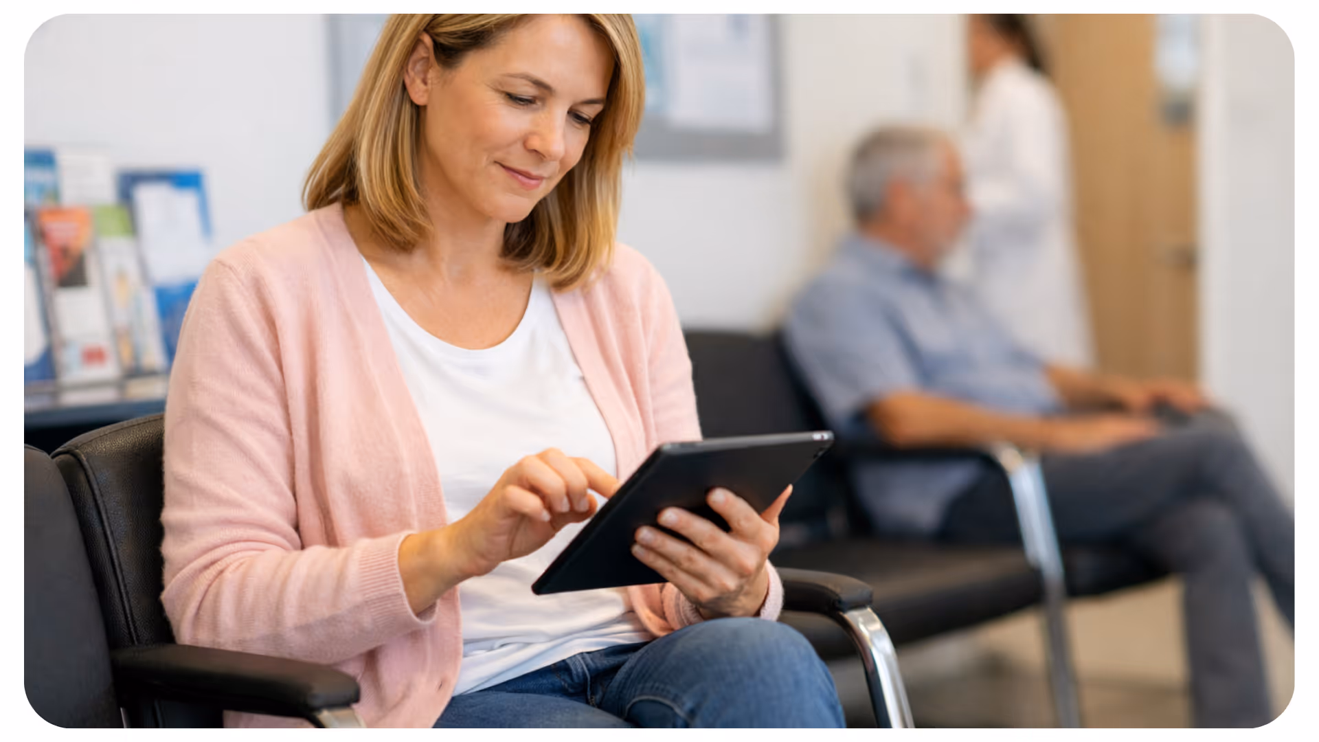 Frau in rosa Cardigan sitzt auf einem Stuhl und tippt am Tablet.