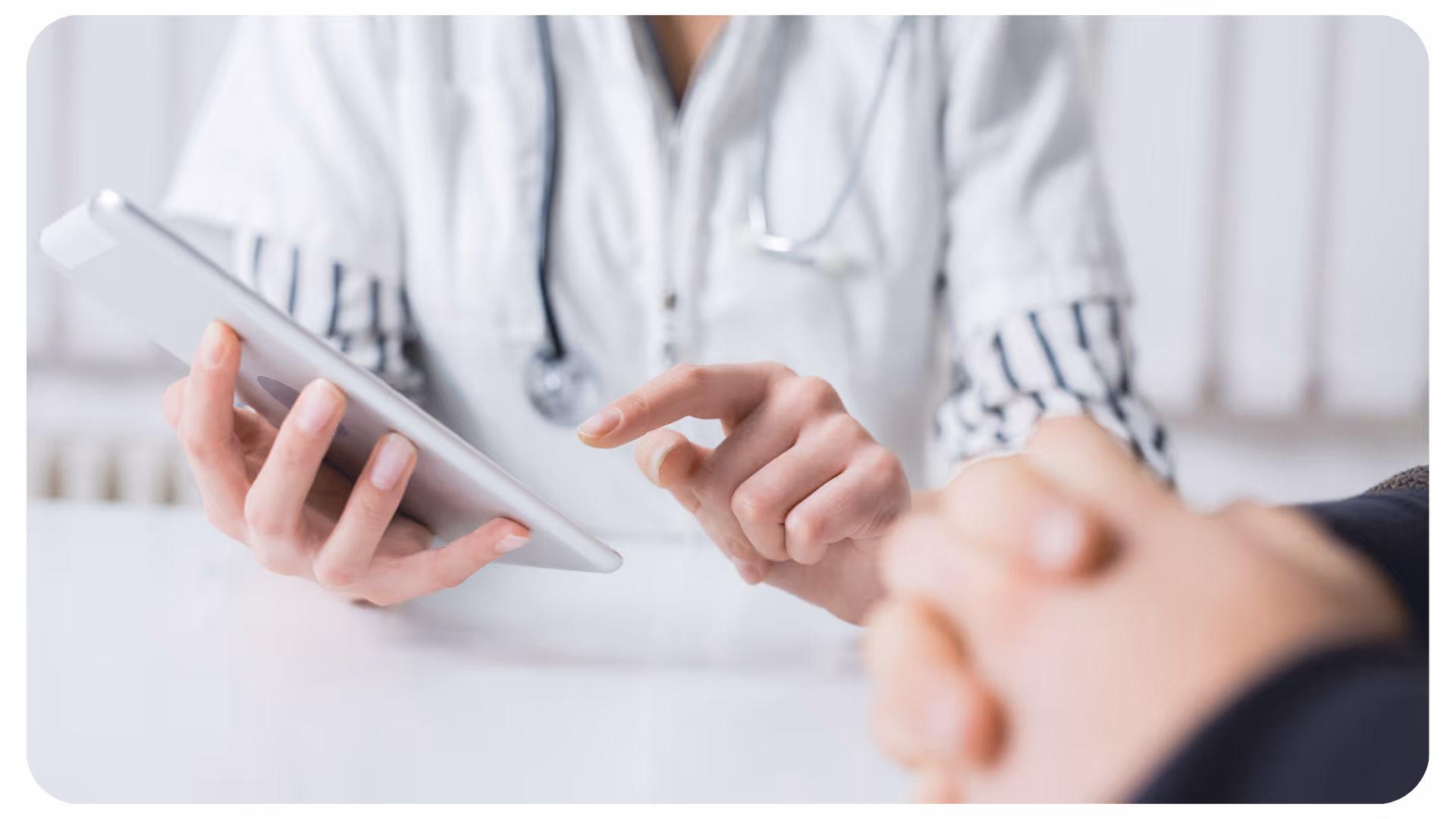 Arzt mit weißem Kittel und Stethoskop zeigt auf ein Tablet, im Vordergrund Hände eines Patienten gefaltet