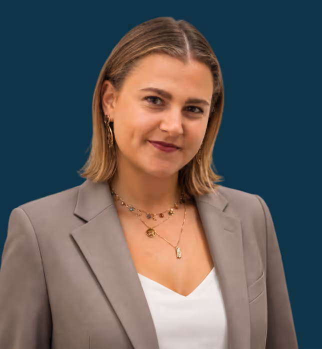 Eine Frau mit schulterlangen hellbraunen Haaren und einem grauen Blazer vor einem blauen Hintergrund