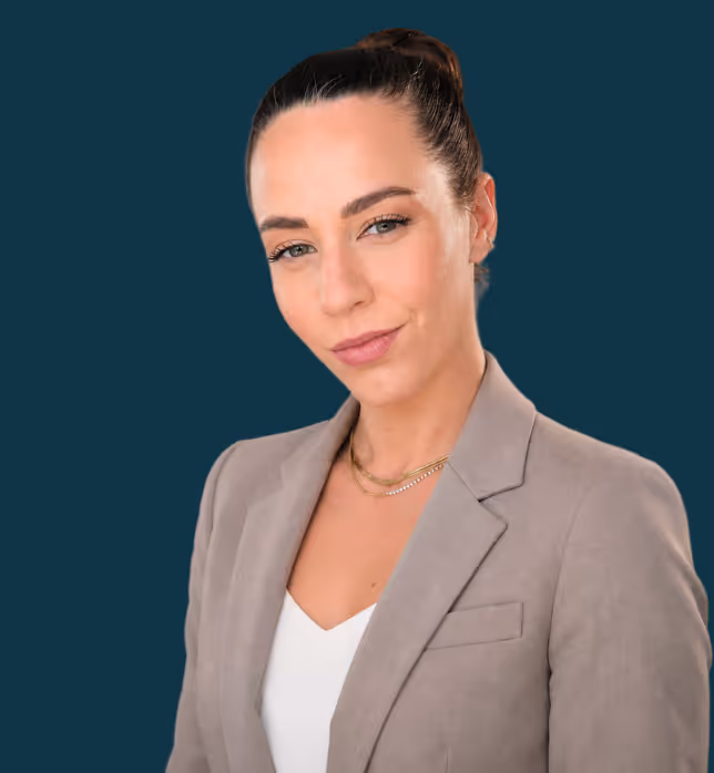 Eine junge Frau mit hochgebundenen braunen Haaren und einem grauen Blazer vor einem blauen Hintergund
