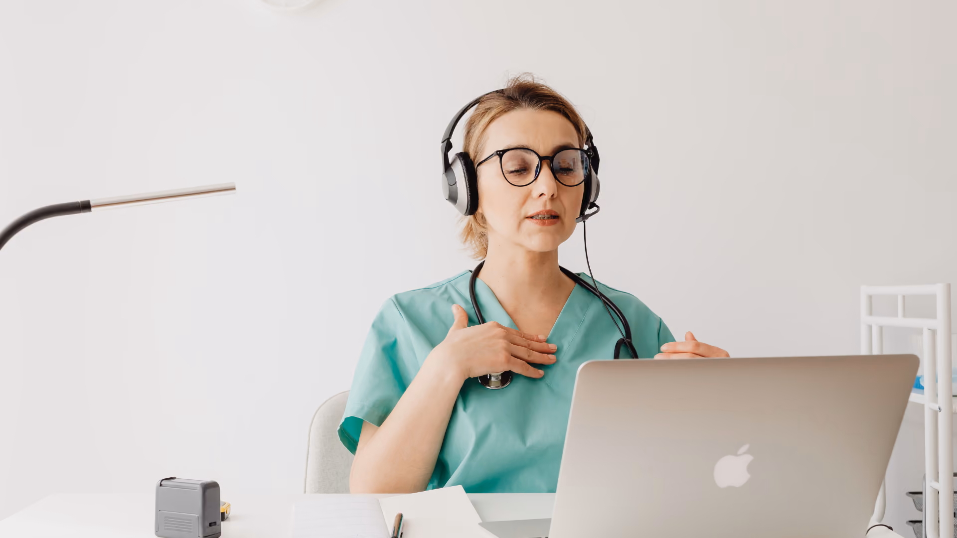 Person mit Headset und türkisem Oberteil sitzt vor Laptop und hebt die Hand