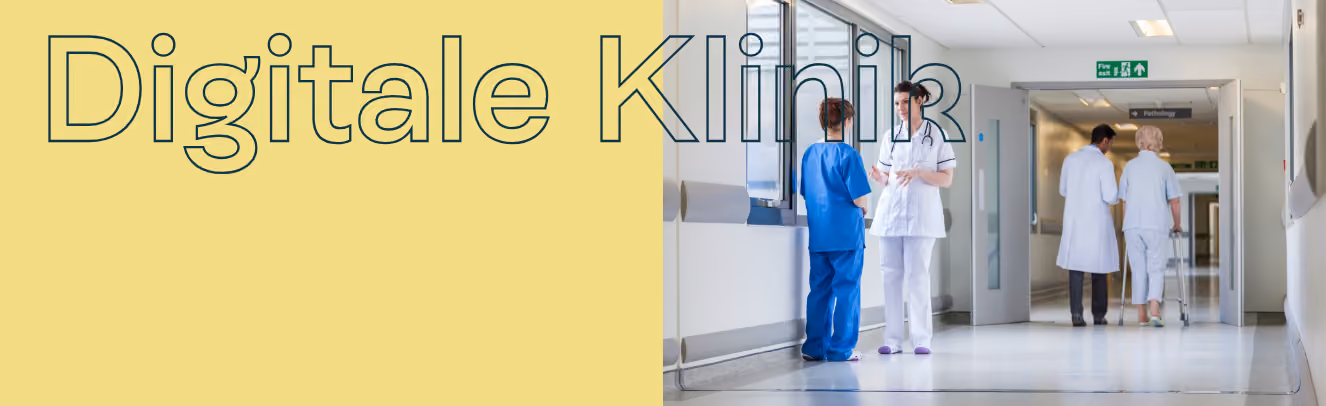 In einem Flur einer Klinik unterhalten sich eine Ärztin und MFA. Im Hintergrund begleitet ein Arzt eine Patientin mit Rollator.
