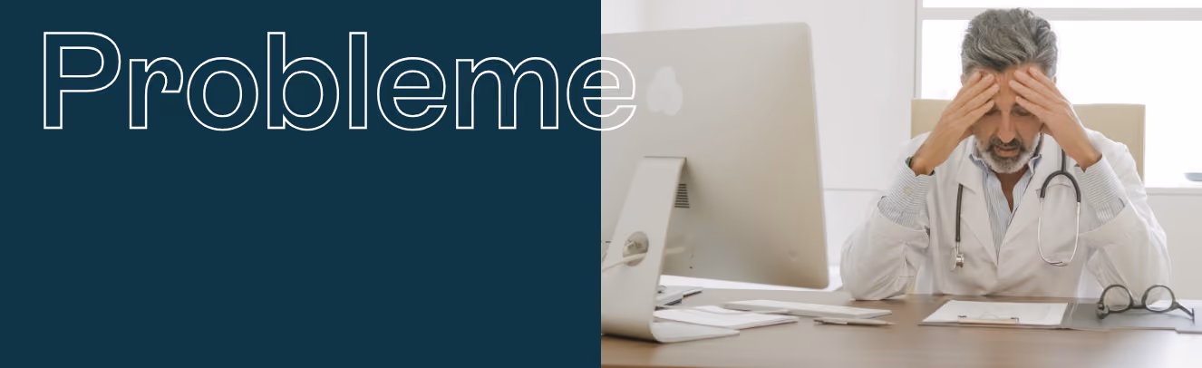 Ein Arzt sitzt an einem Schreibtisch vor einem Computer und hält sich mit beiden Händen den Kopf.