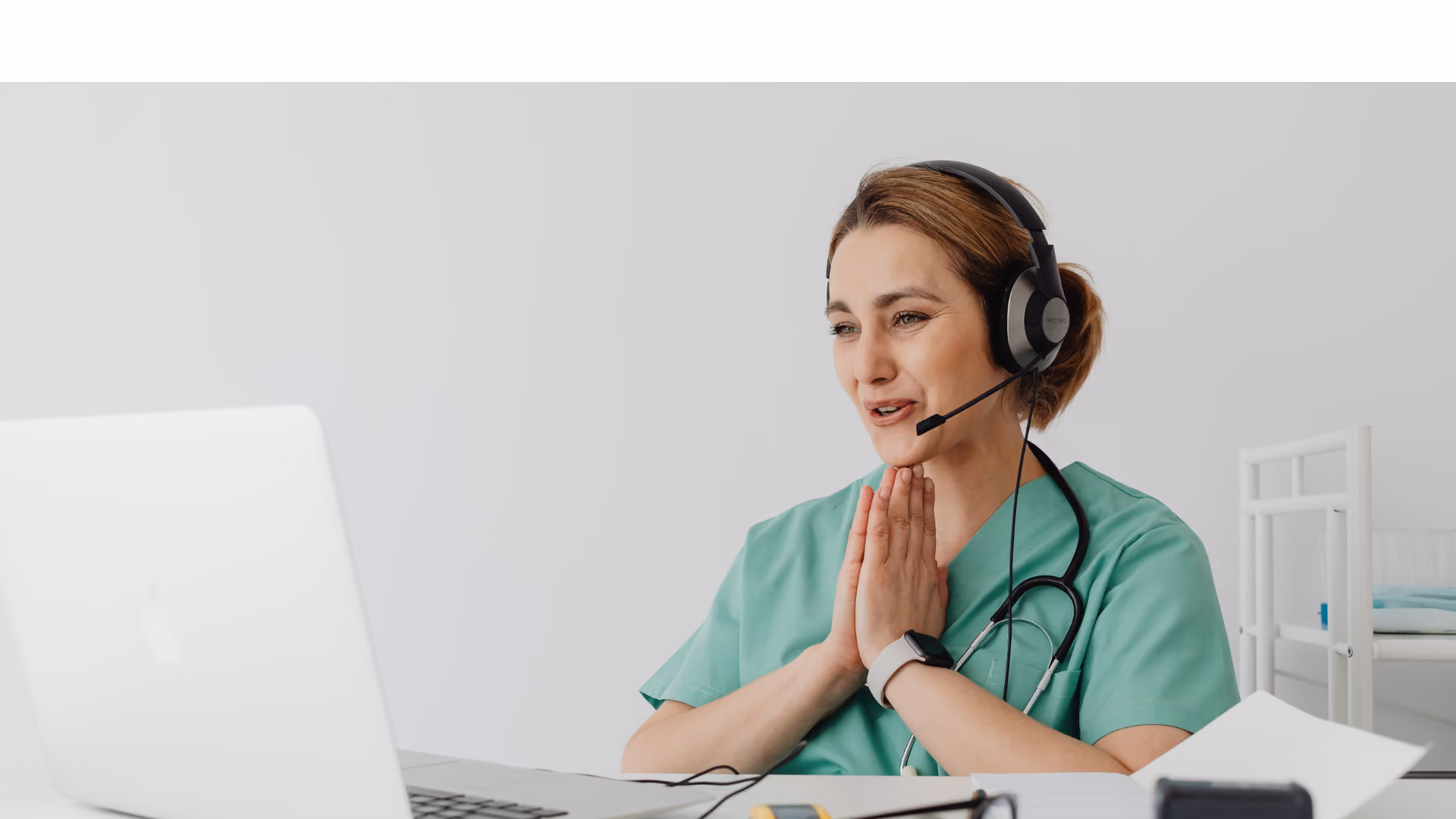 Person mit Headset sitzt vor einem Laptop und hat die Hände gefaltet