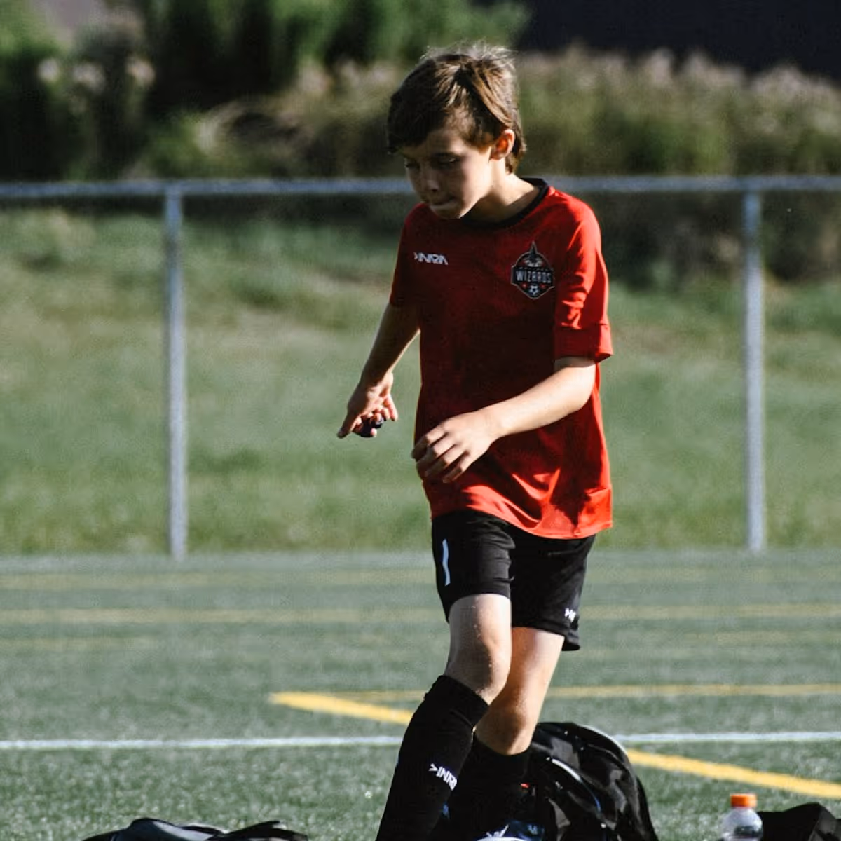 Young boy in a red Wizards soccer jersey and black shorts standing on a soccer field.