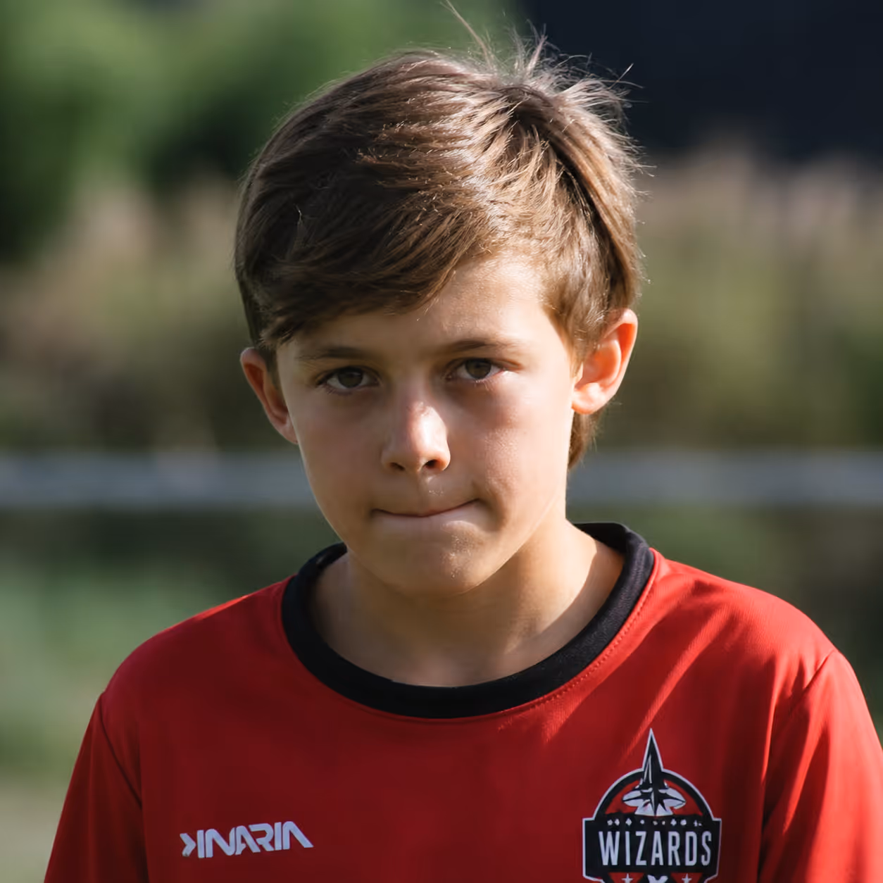 Portrait of a boy wearing a red Wizards sports jersey with a focused expression outdoors.