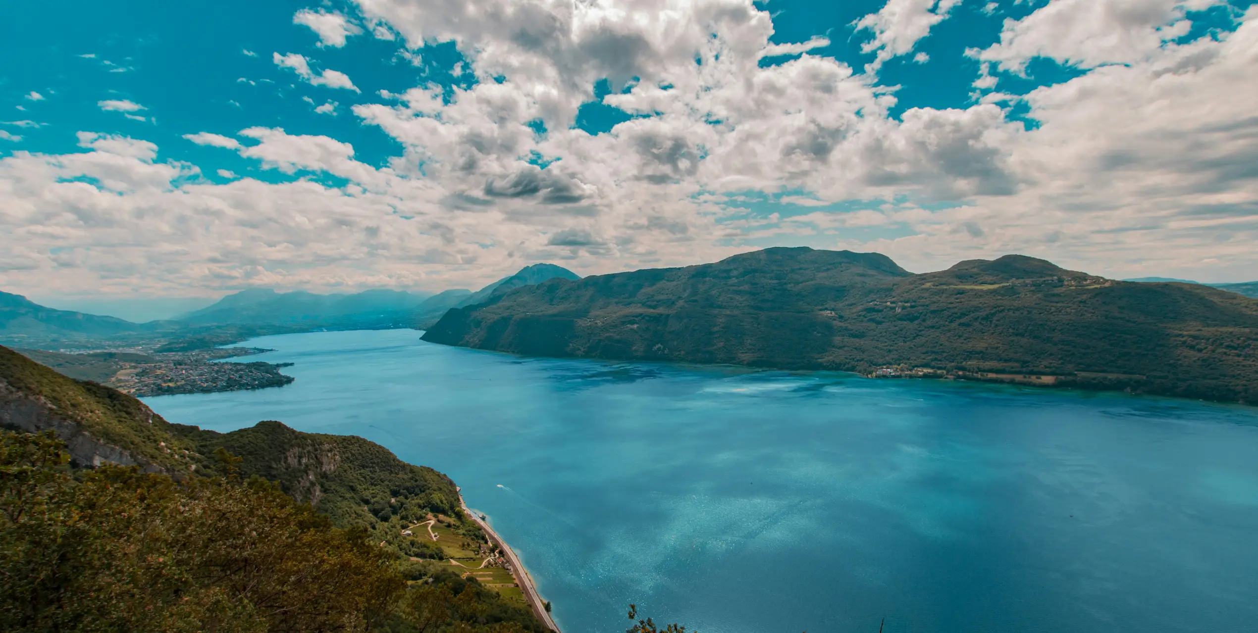 Wide blue lake surrounded by green mountains under a partly cloudy sky.