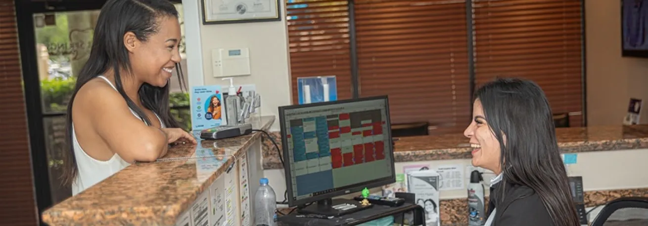 Two women sitting at a counter in front of a computer.