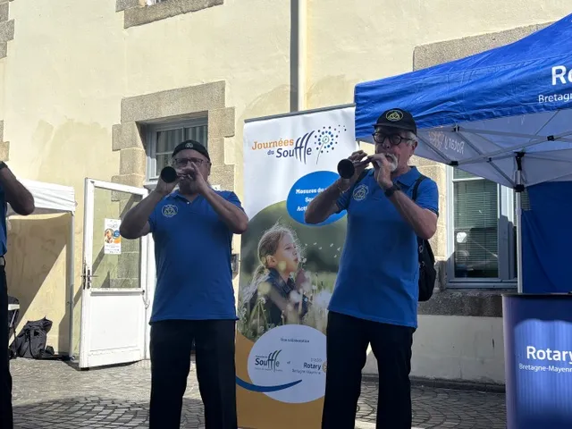 Action de sensibilisation du CNMR, comité national contre les maladies respiratoires, en France. Deux musiciens jouant de la bombarde devant une tente Rotary lors d'un stand en extérieur.