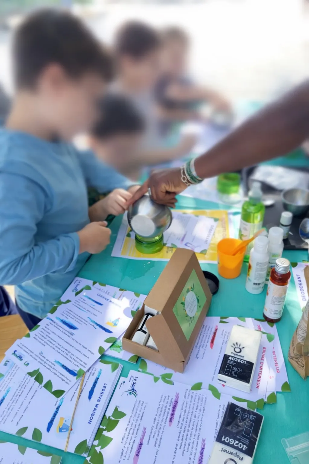Action de sensibilisation du CNMR, comité national contre les maladies respiratoires, en France. Enfants participant à un atelier versant un liquide dans un pot sur une table avec produits écologiques.