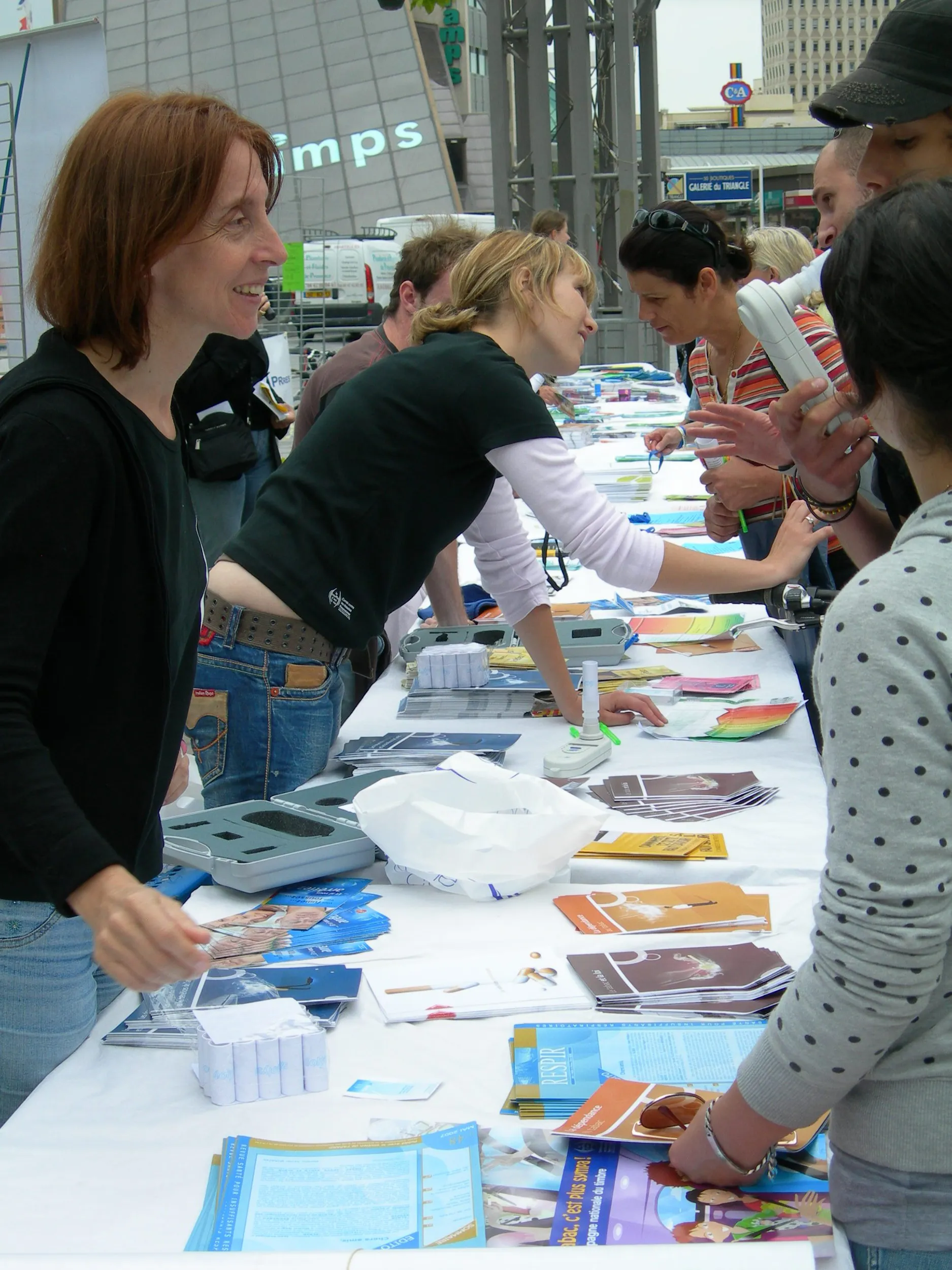 Action de sensibilisation du CNMR, comité national contre les maladies respiratoires, en France. Des personnes discutent et distribuent des brochures à une table lors d'un événement en plein air.