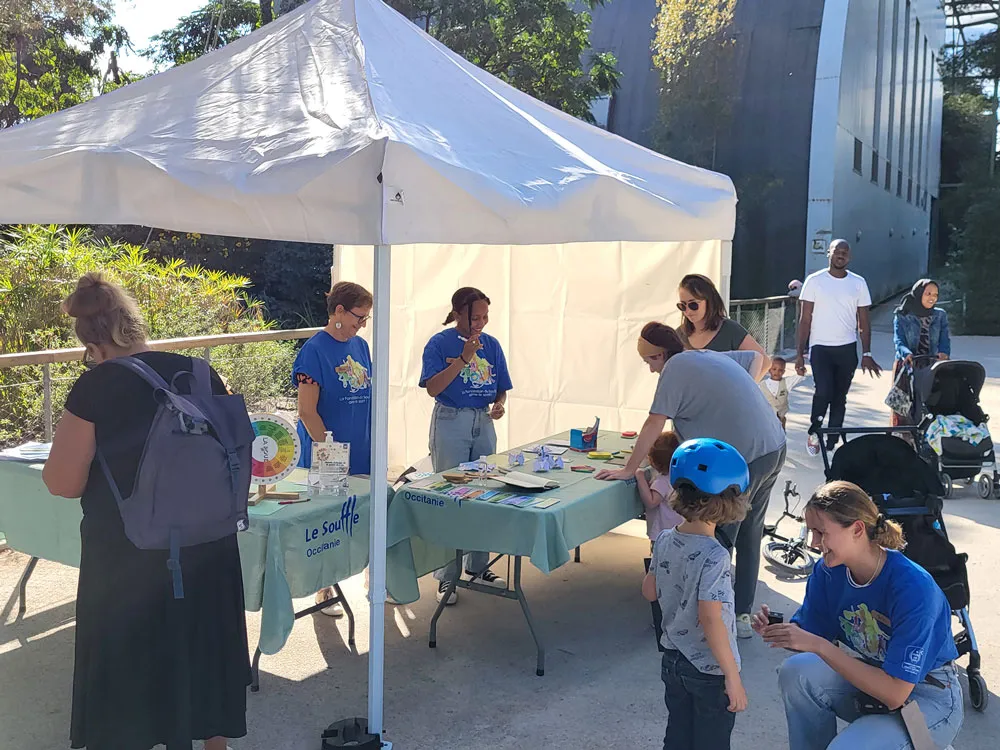 Action de sensibilisation du CNMR, comité national contre les maladies respiratoires, en France. Stand en plein air avec personnes, enfants jouant, et intervenants en tee-shirts bleus sous un auvent blanc.