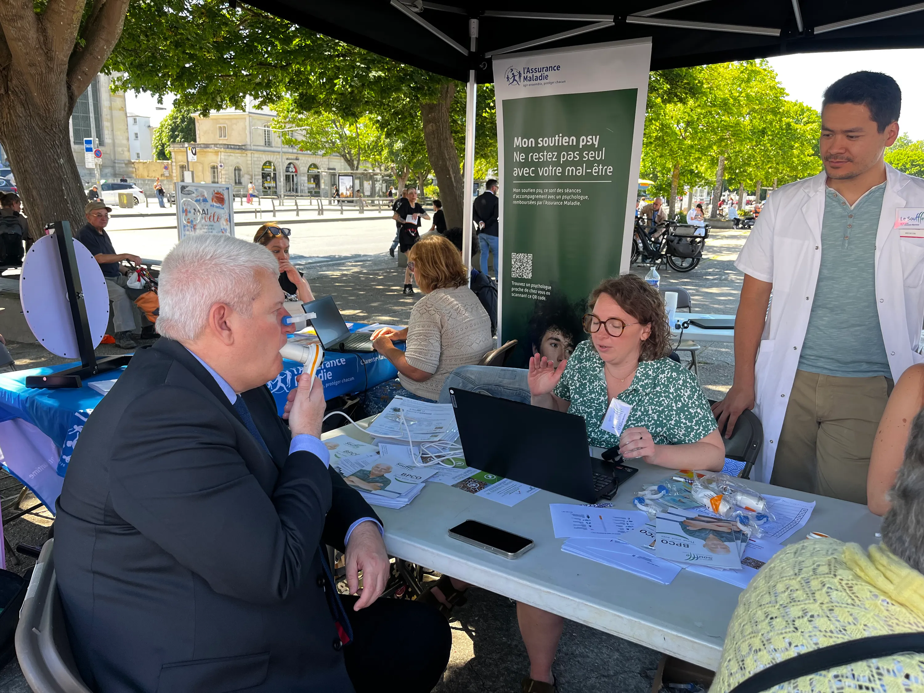 Action de sensibilisation du CNMR, comité national contre les maladies respiratoires, en France. Un homme fait un test respiratoire à une table d'information en plein air avec du personnel médical.