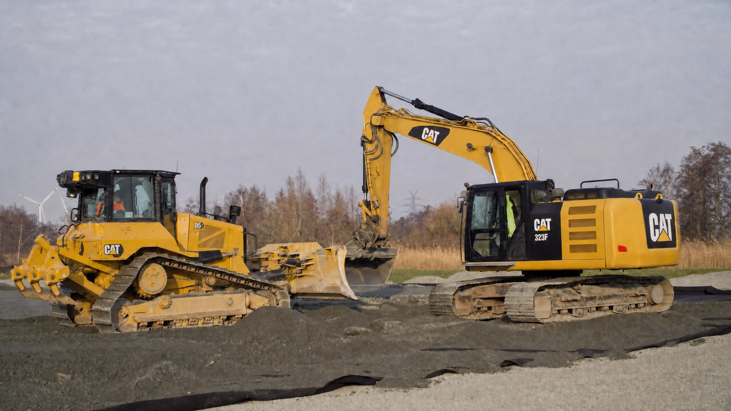 Zwei gelbe CAT-Bagger arbeiten auf einer Baustelle mit Kies und Erde.