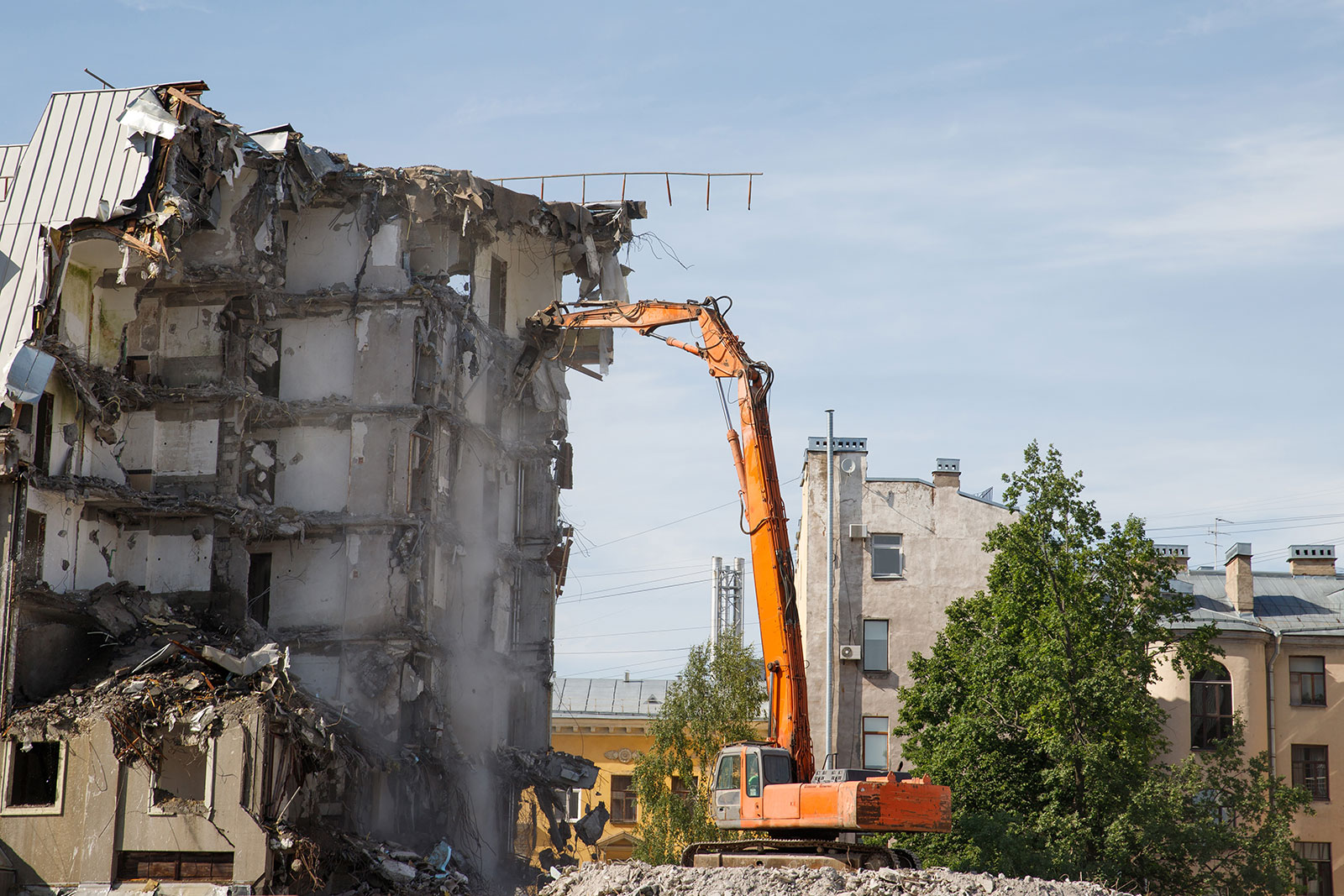 Orange excavator demolishing a multi-story concrete building with debris on the ground.