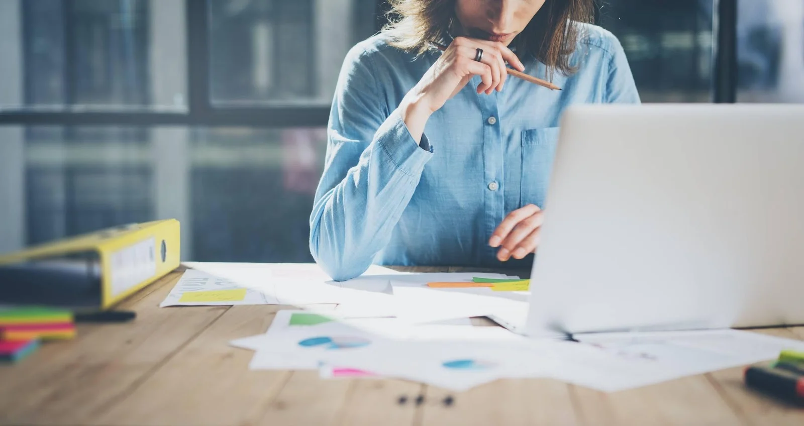 Une entrepreneuse définit les avantages concurrentiels de son entreprise. Son bureau est couvert de feuilles et de son ordinateur portable.