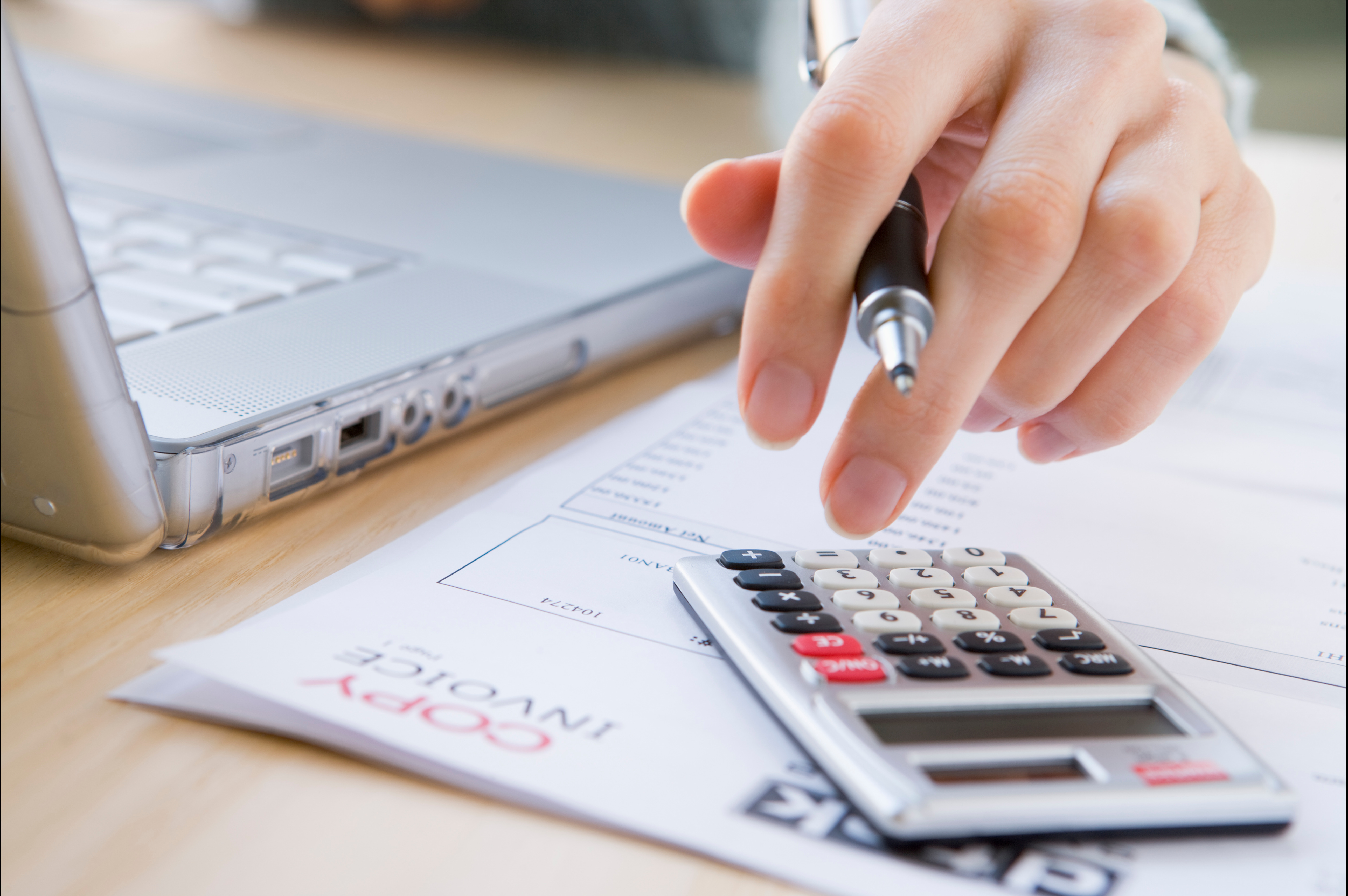 Réduire délais de paiements. Une image illustrant un comptable devant son ordinateur, effectuant des calculs à l'aide d'une calculatrice