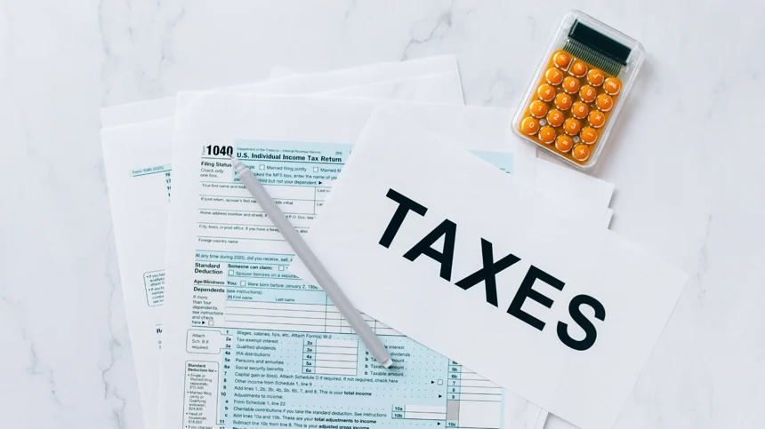 TVA declaration. Une image illustrant des factures et une calculatrice posées sur une table, avec le mot "taxe" écrit sur une feuille.
