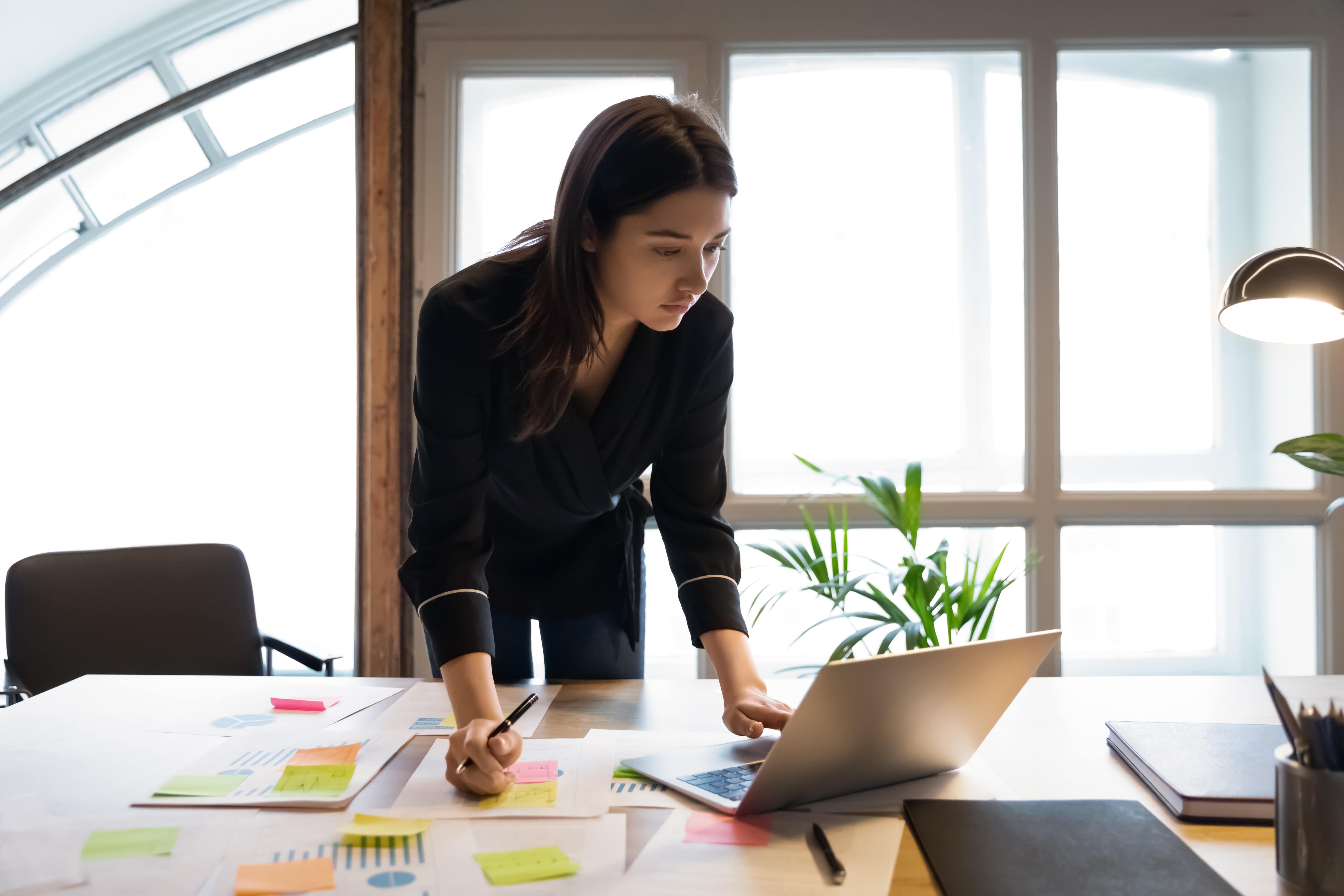 Une entrepreneure fait un plan de financement pour son entreprise depuis son bureau couvert de post-its. 