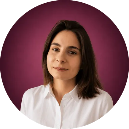 Portrait d'une femme souriante aux cheveux bruns et chemise blanche sur fond rose foncé.