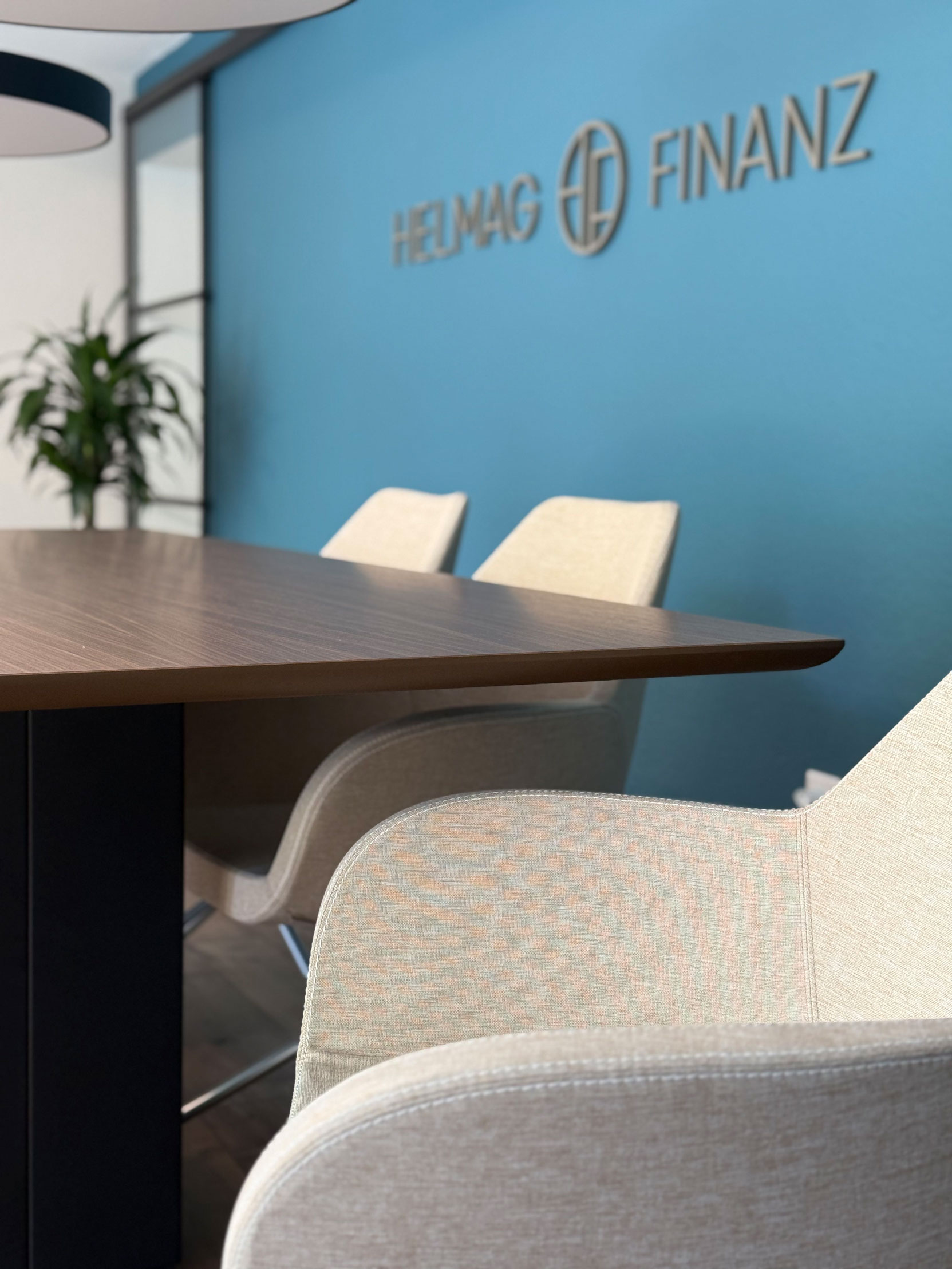 Konferenzraum mit braunem Tisch, beige Stühlen und blauem Wand mit der Aufschrift ‚HELMAG FINANZ‘.
