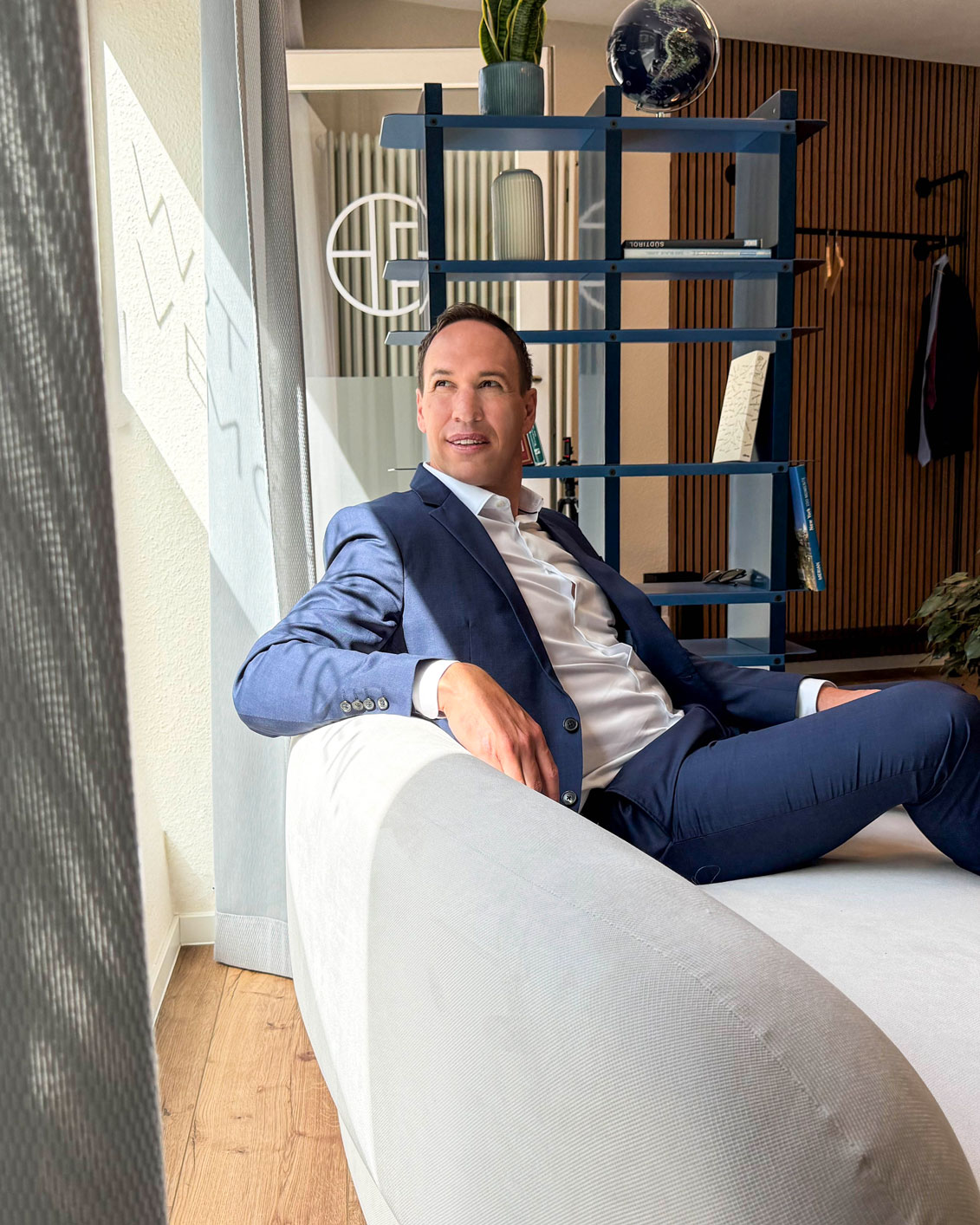 Mitarbeiterin mit kurzen blond-braunen Haaren, Brille und einem blaugrünen Blazer, die in einem Büro am Computer arbeitet.