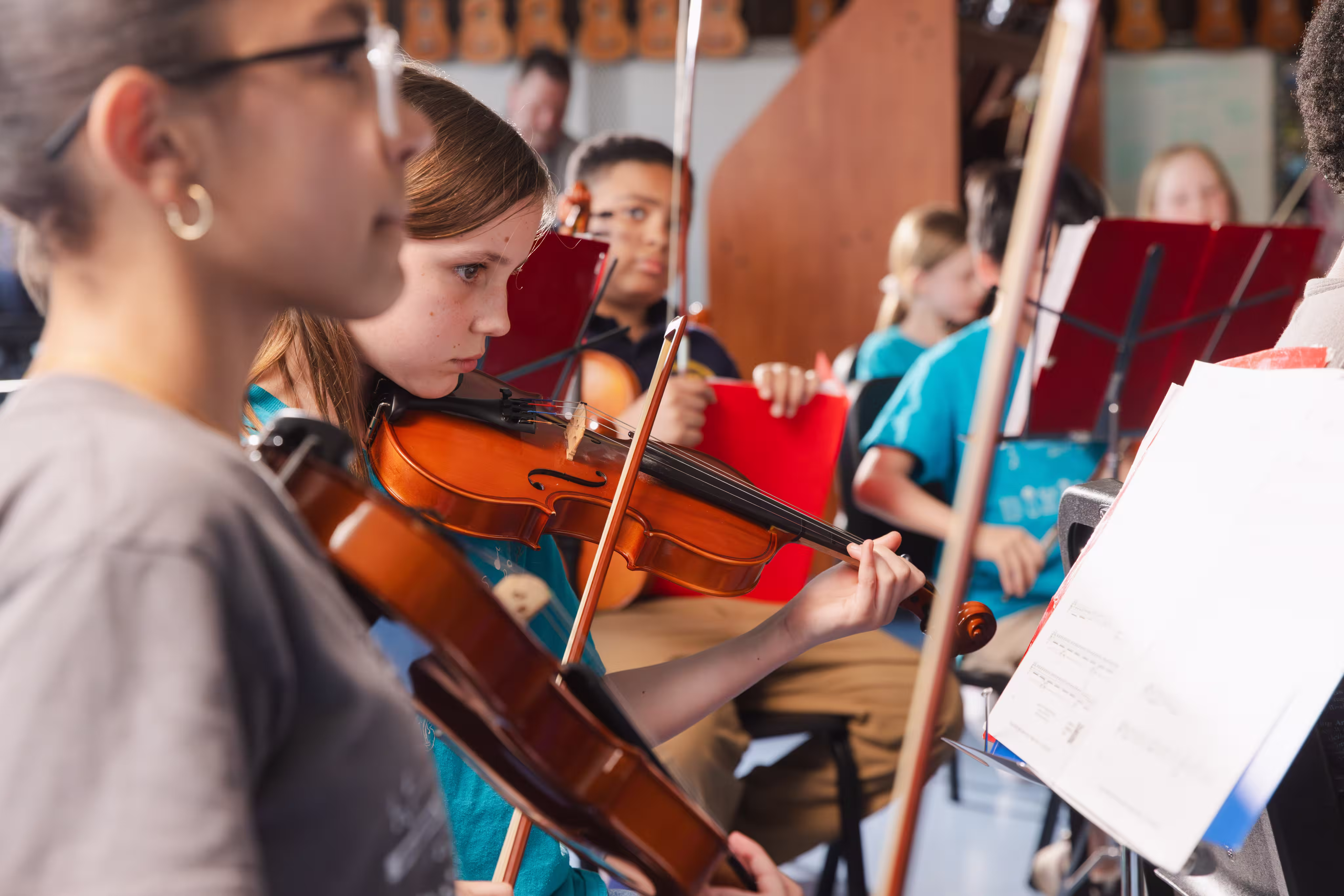 Group of children playing violins in a music class with focused expressions and sheet music on stands.