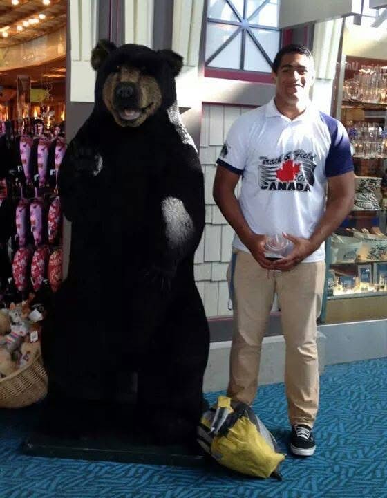 Man in white Canada t-shirt standing next to a large black bear statue inside a store.