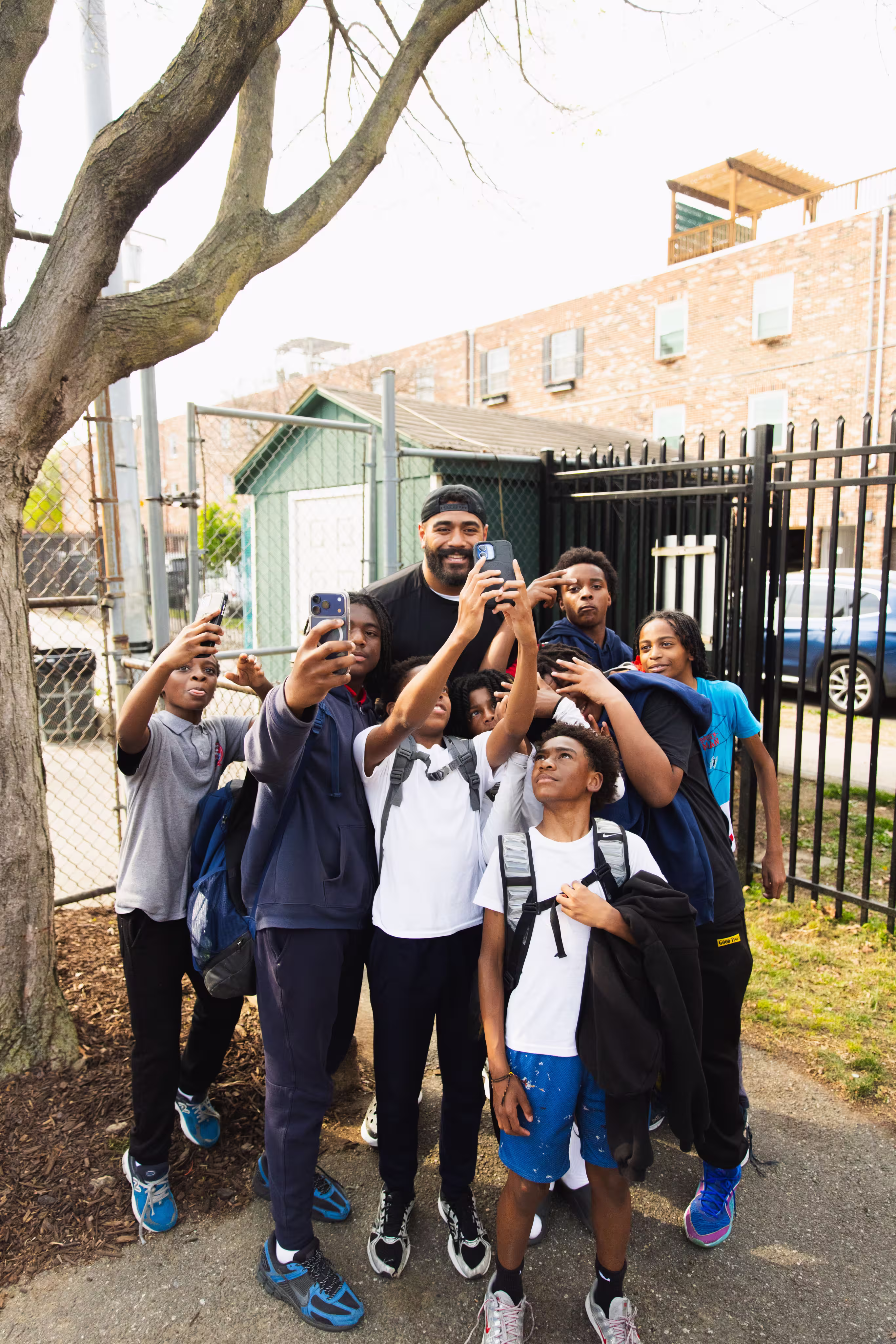 Group of boys with backpacks and a man smiling as they take multiple selfies outdoors.