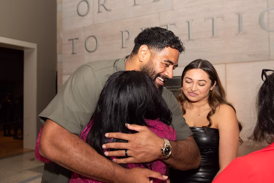 Man in green shirt happily hugging a woman in a sparkly pink dress with two others nearby.