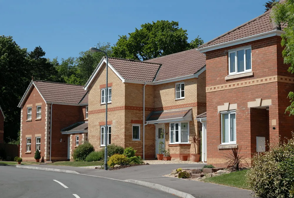 Modern suburban brick houses on a curved street with a clear blue sky and green trees.