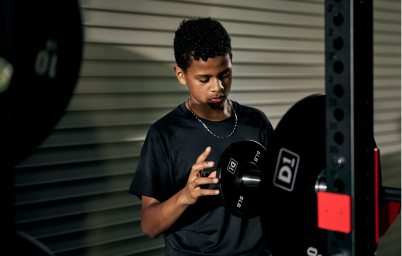 Young man in black shirt holding a weight plate in a gym setting near workout equipment.