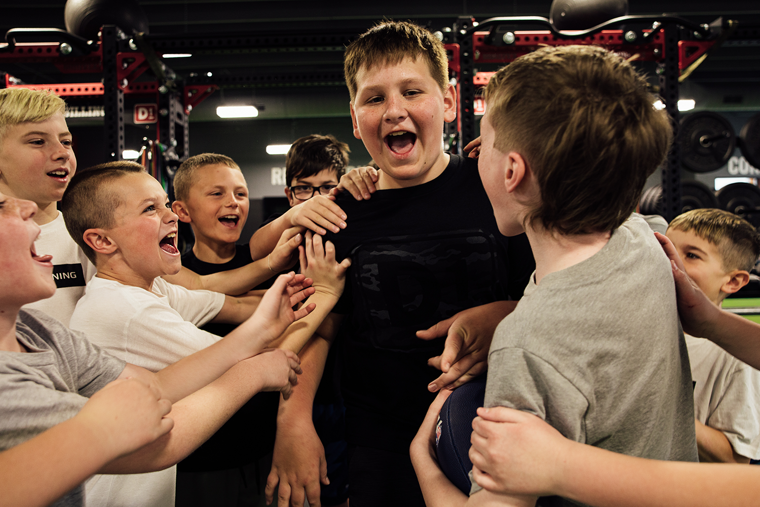 Group of excited boys in a gym celebrating and cheering with one boy in the center smiling loudly.