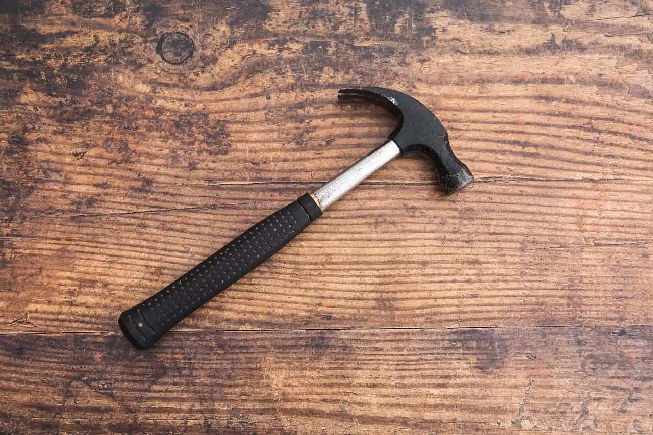 A black-handled hammer resting diagonally on a weathered wooden surface, evoking themes of work, value, and practical wisdom — possibly symbolizing grounded insights from a Money Workshop.
