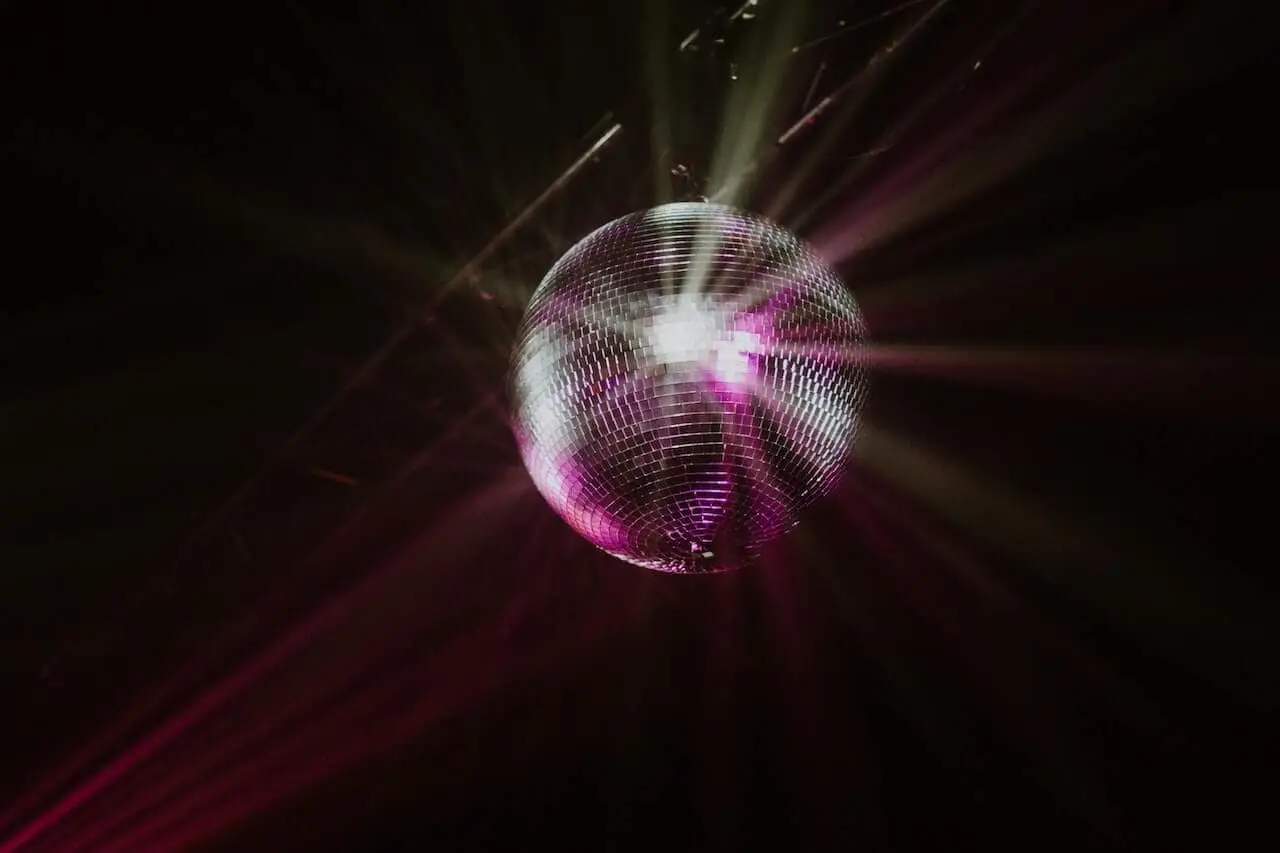 Mirror disco ball reflecting pink and white light across a dark space, creating radiating beams of light.