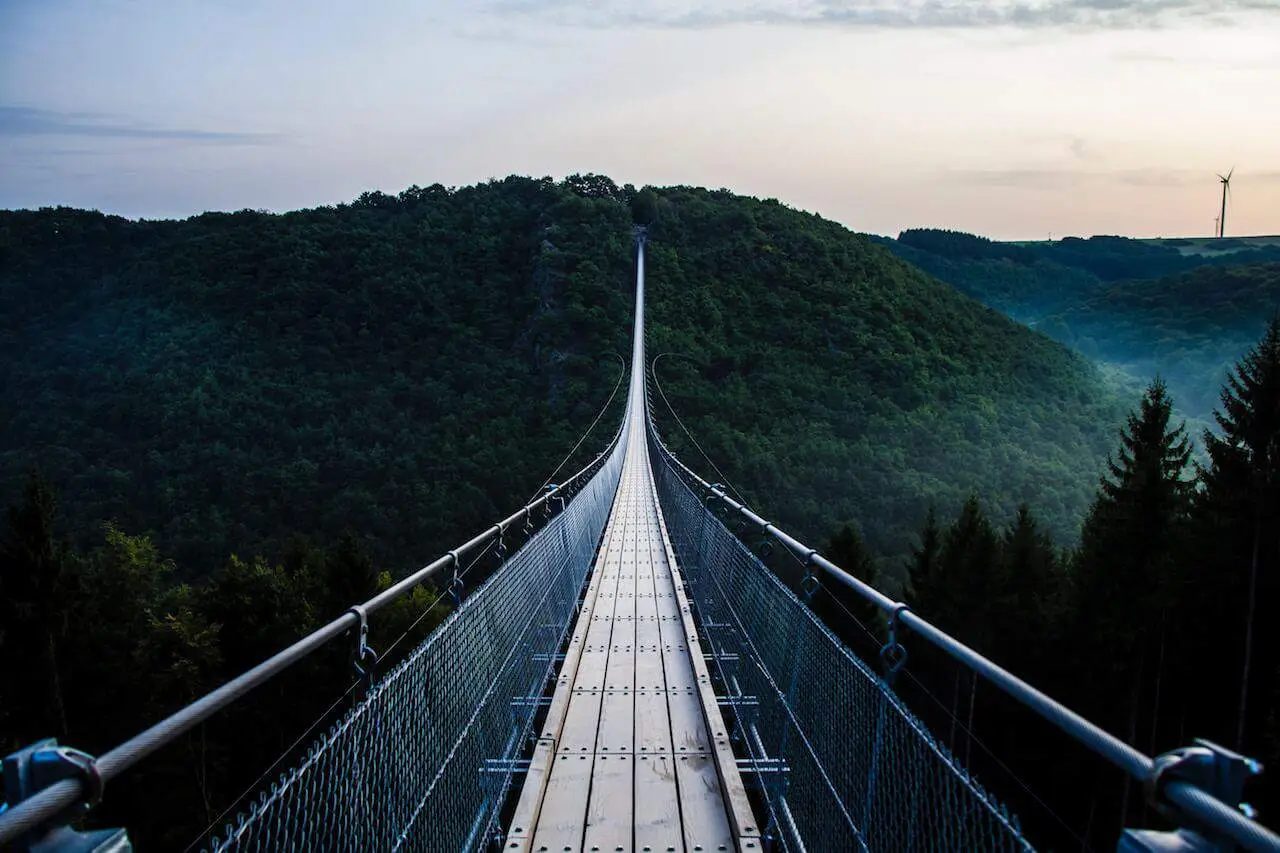 Suspension bridge stretching into a forested mountain, symbolising the journey through uncertainty toward a new path or purpose.