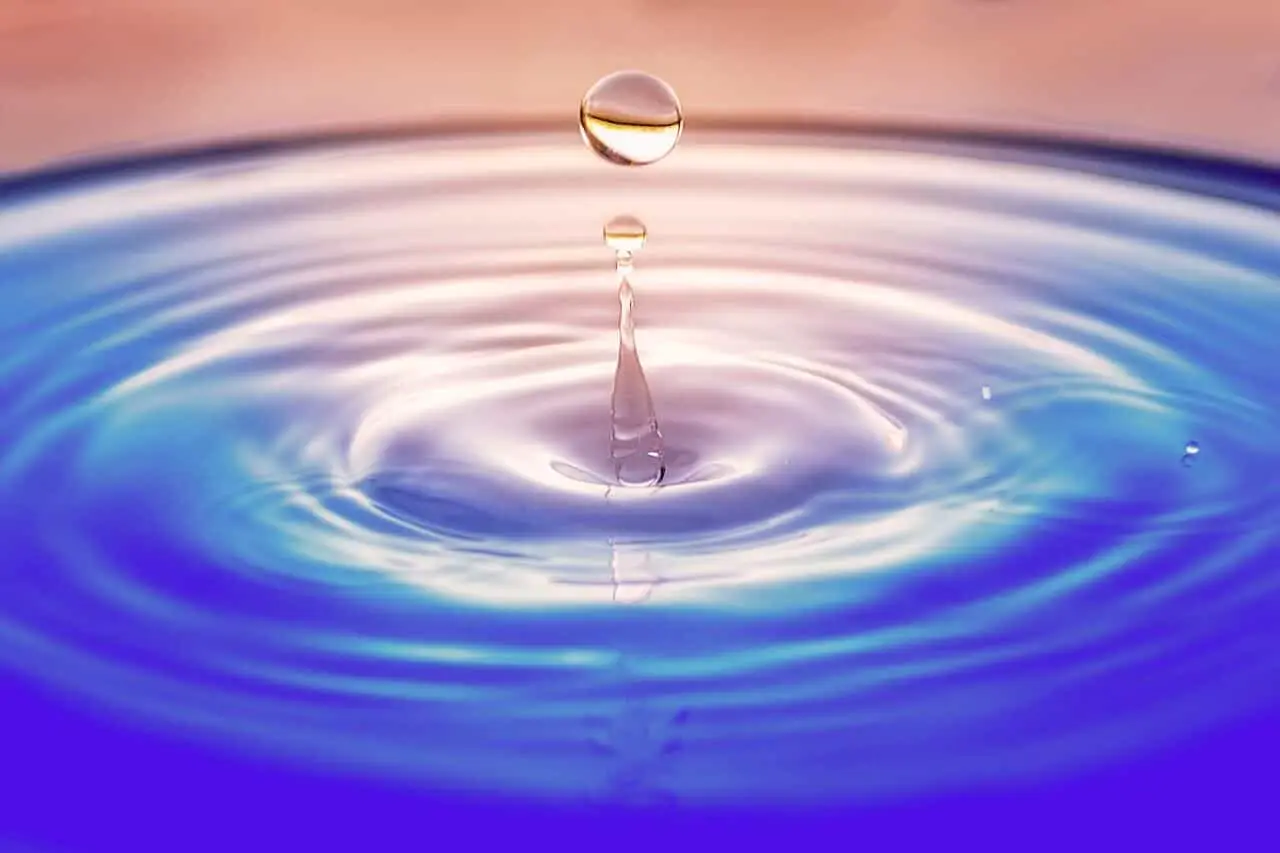 A single water droplet rises above a calm surface, surrounded by concentric ripples—capturing the essence of how small actions radiate outward in all directions.