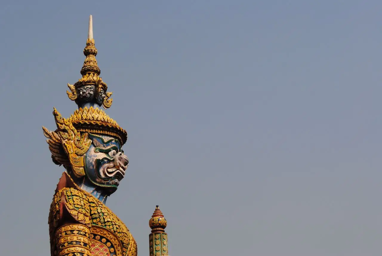 A vibrant, ornate guardian statue with a fierce expression and golden armour, standing watch beneath a clear sky—embodying protection, boundaries, and spiritual vigilance at the edge of sacred space.
