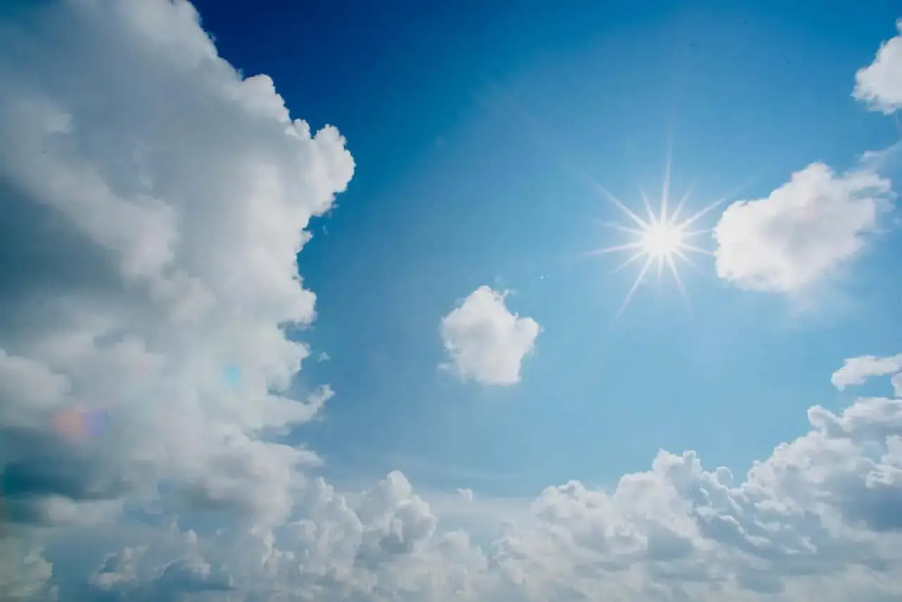 Bright sun shining in a clear blue sky, surrounded by fluffy white clouds.