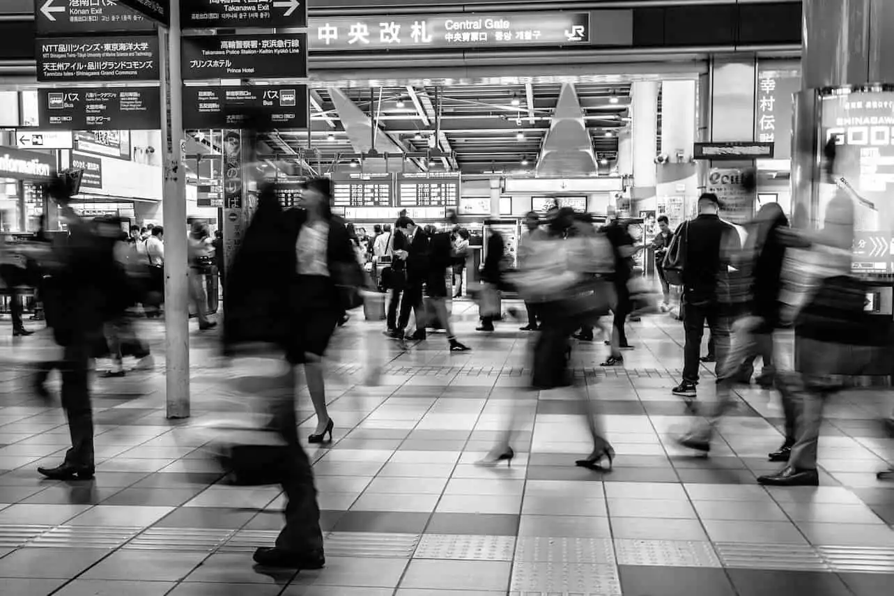 Black and white photo of a busy train station with blurred figures walking, capturing the rush of commuters in motion.