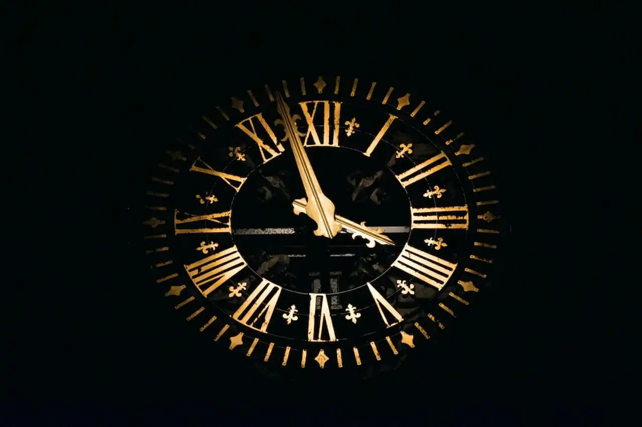 A large, ornate clock face with gold Roman numerals and hands against a black background, showing the time at just before 4 o'clock.
