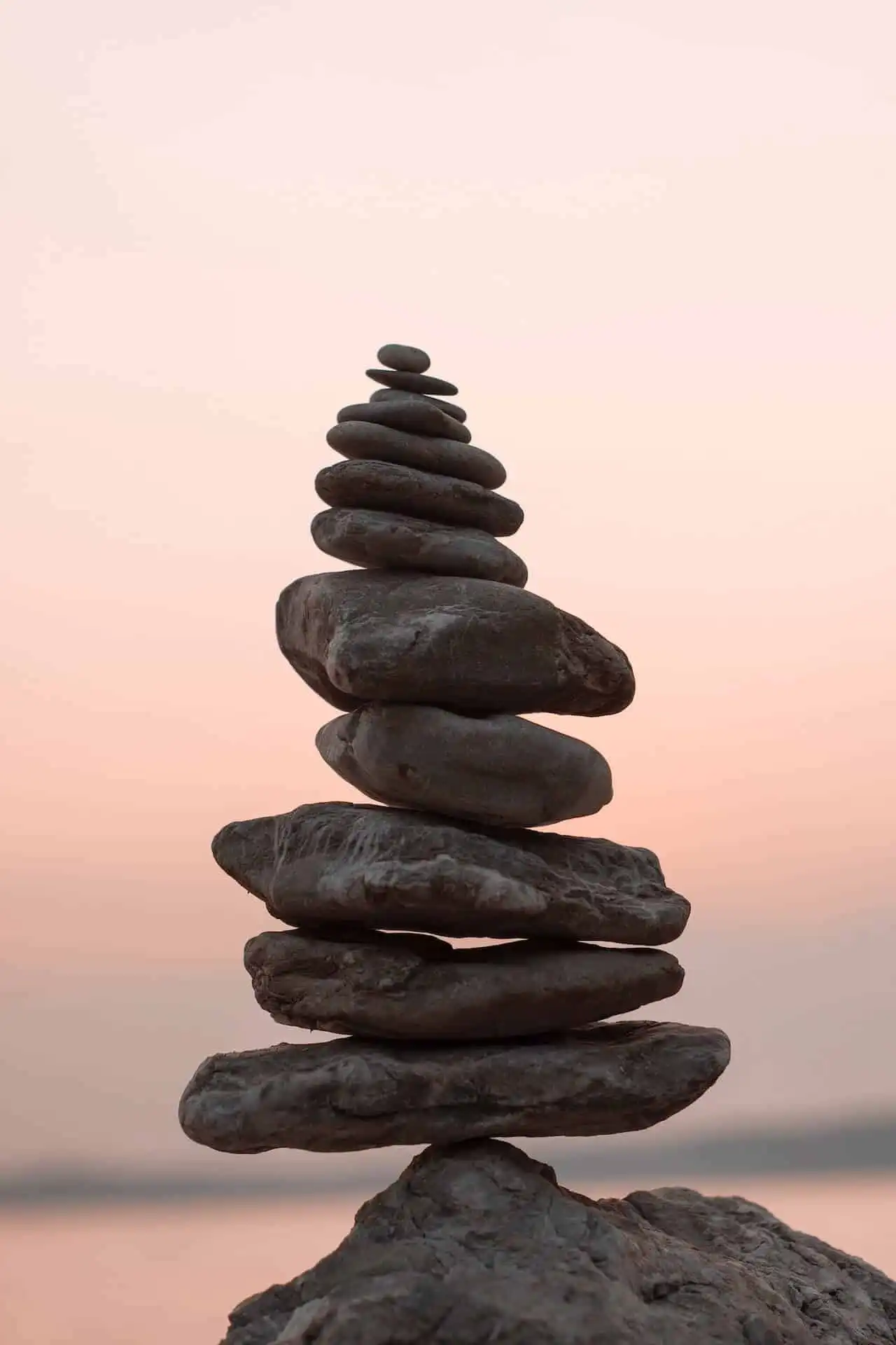 A tall, carefully balanced stack of smooth, flat stones against a soft pastel sky at sunset.