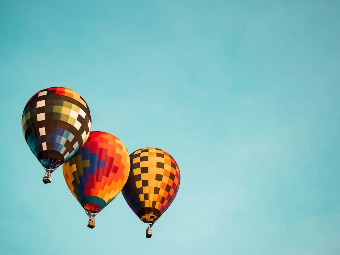 Three colorful hot air balloons with checkered patterns floating in a clear blue sky, symbolizing freedom and lightness.