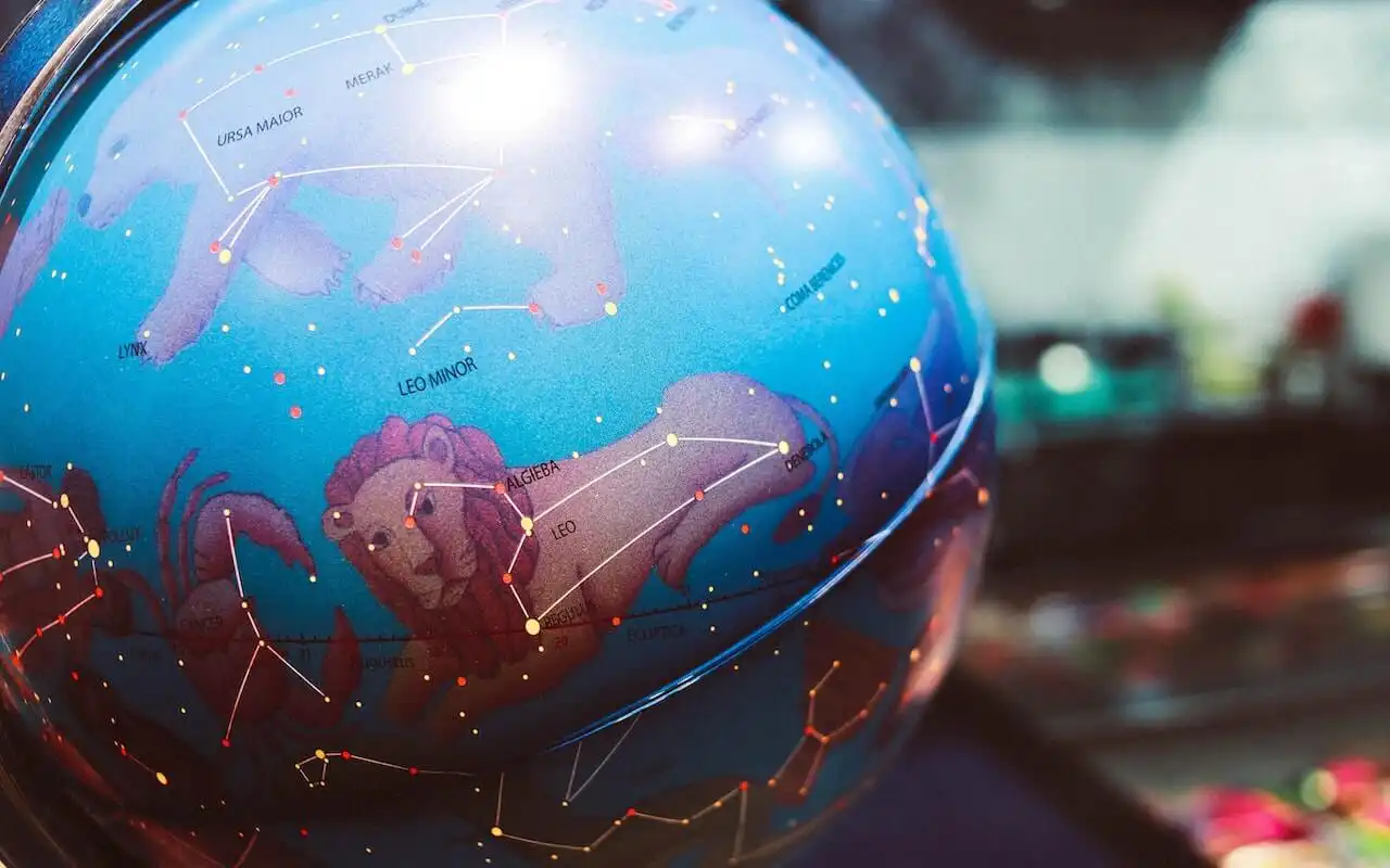 Close-up of a celestial globe displaying constellations, including Leo, Leo Minor, and Ursa Major, with illustrated zodiac symbols and star patterns mapped in vibrant colors on a blue background.