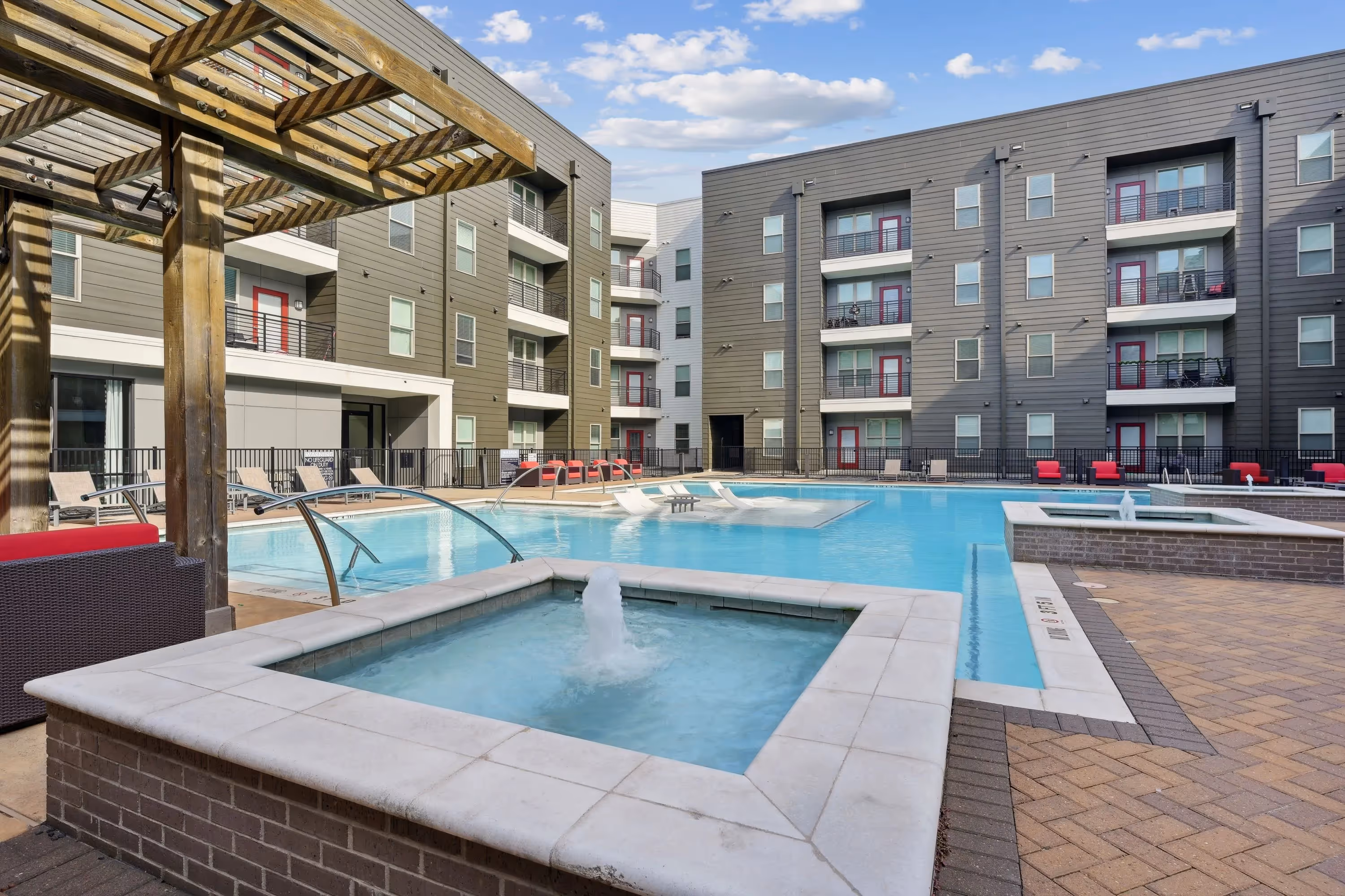 Resort-style swimming pool and hot tub area with lounge seating, surrounded by modern apartment buildings, at Altitude in Houston, TX.